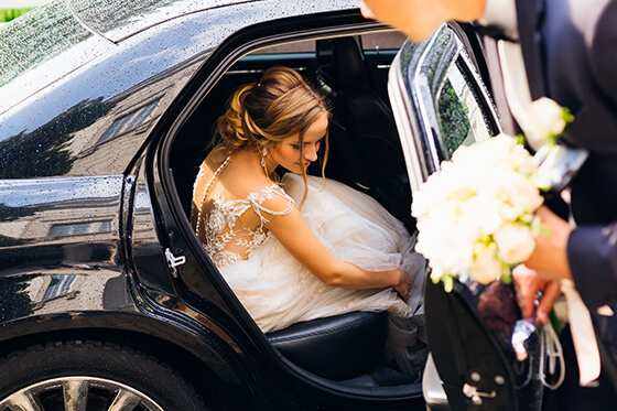 Eine Braut sitzt in einer Hochzeitslimousine und ein Chauffeur öffnet ihr die Tür.