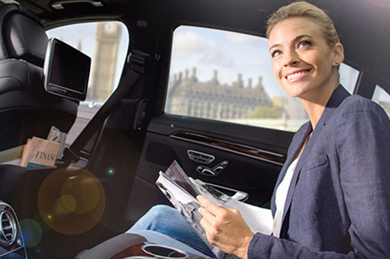 A woman sitting in a limousine reading a newspaper.