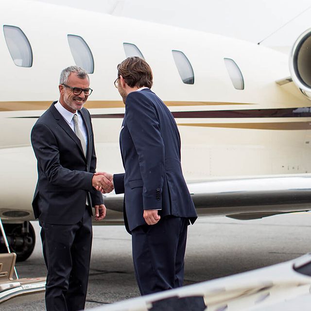 A chauffeur is shaking hands with a customer in front of an airplane.