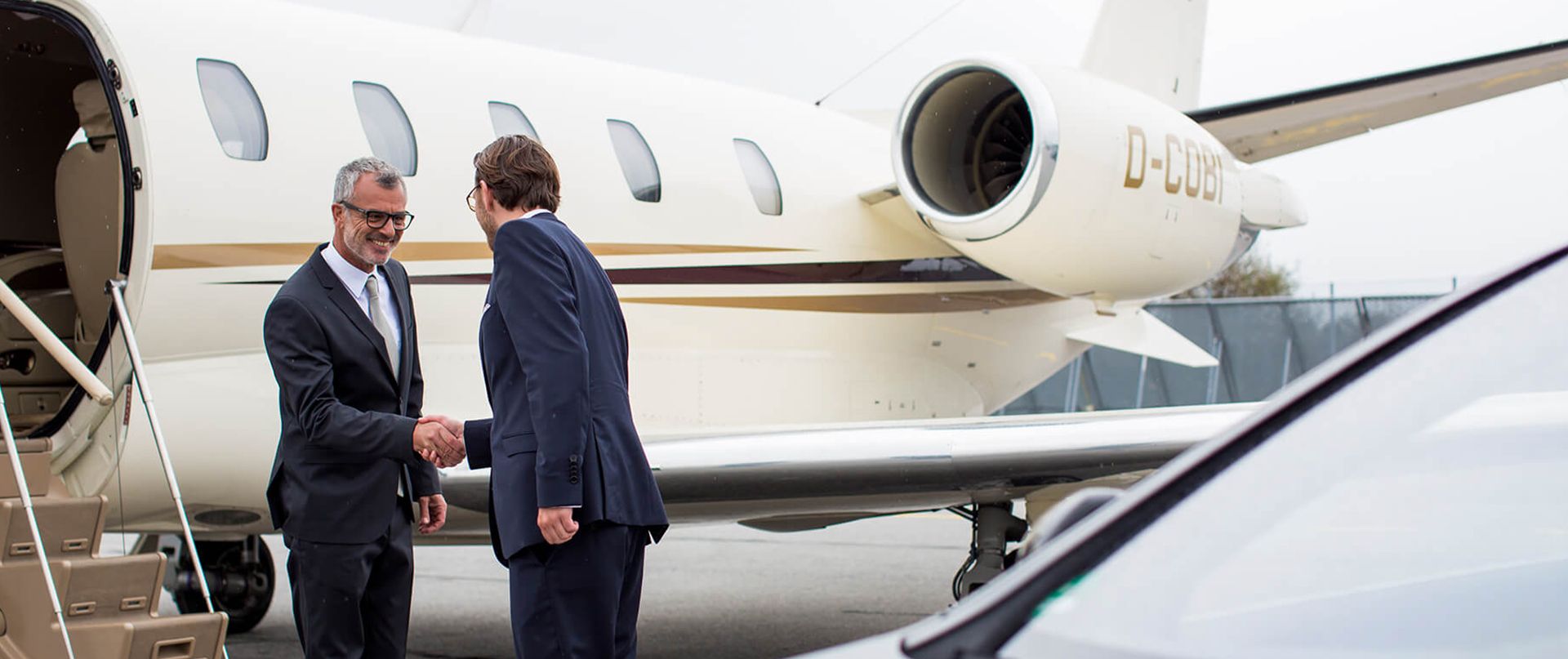 A chauffeur is shaking hands with a customer in front of an airplane.