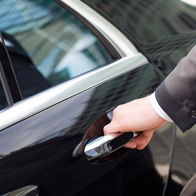 A chauffeur opens the door of a limousine.