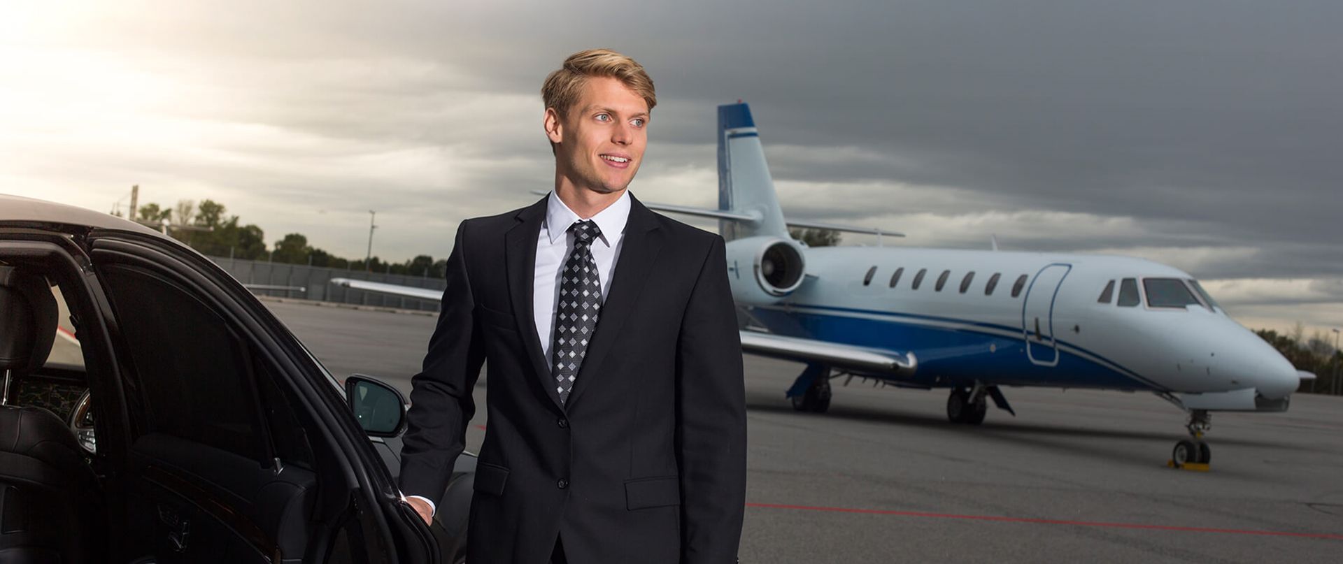 Ein Chauffeur vor einer Limousine und einem Business-Jet.