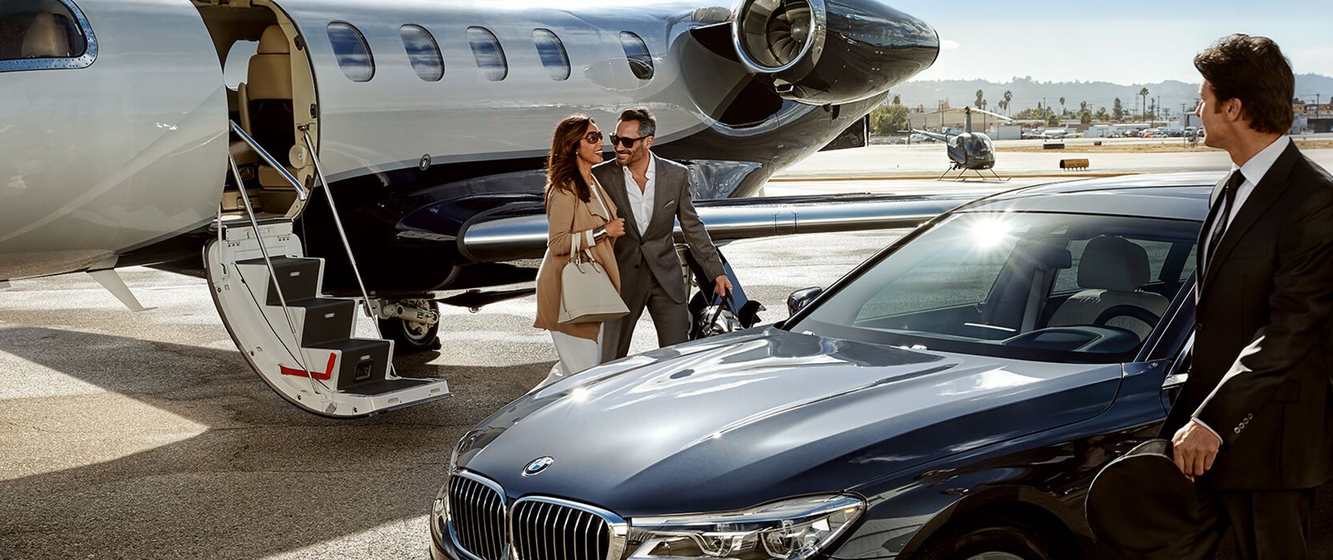 A chauffeur with a limousine picks up a couple in front of a business jet.