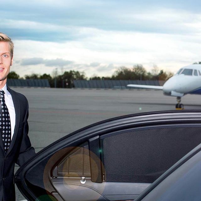 A chauffeur opens the door of a limousine in front of an airplane.