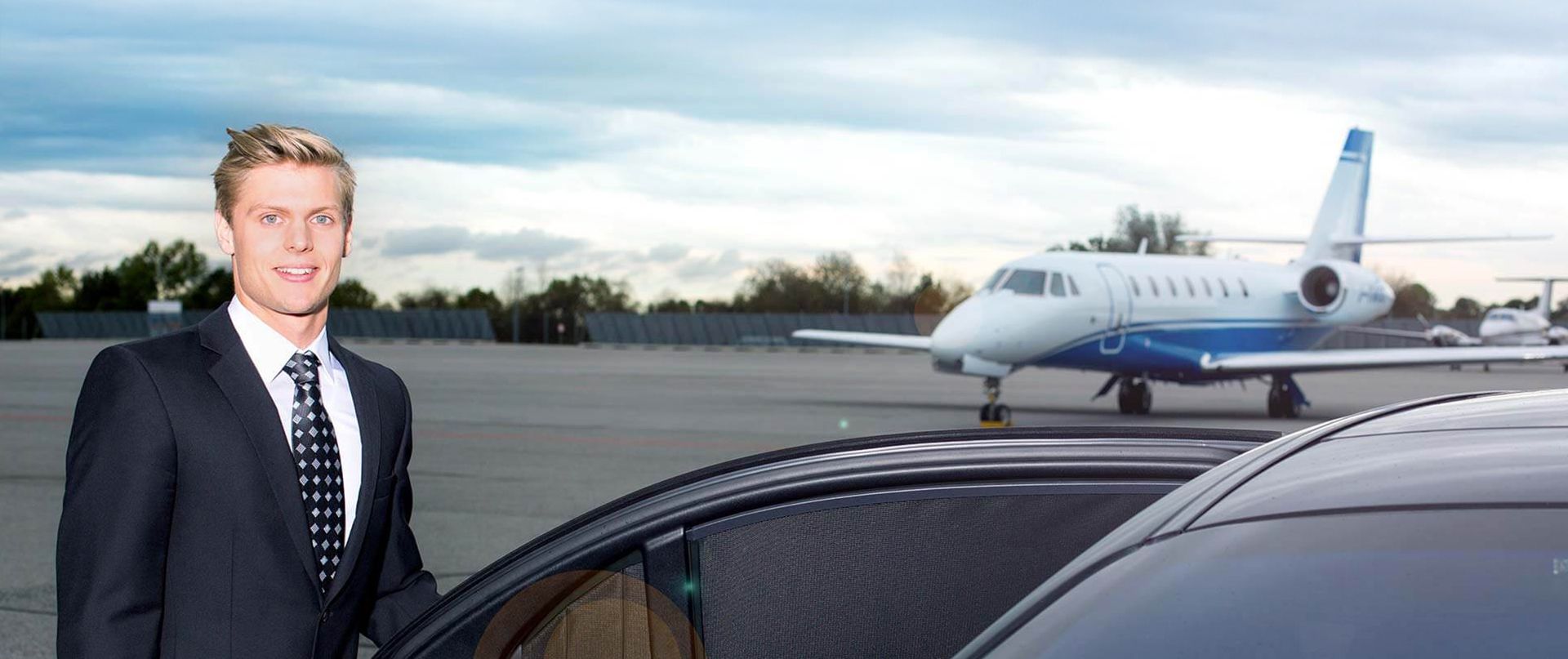 Ein Chauffeur öffnet die Tür einer Limousine auf dem Rollfeld vor einem Business-Jet.