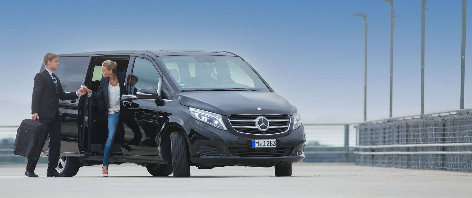 Ein Chauffeur hilft einer Frau aus einem Minivan am Flughafen.